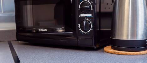 Un horno microondas negro con dos mandos y una pantalla digital, situado sobre una encimera de cocina junto a una cafetera de acero inoxidable.