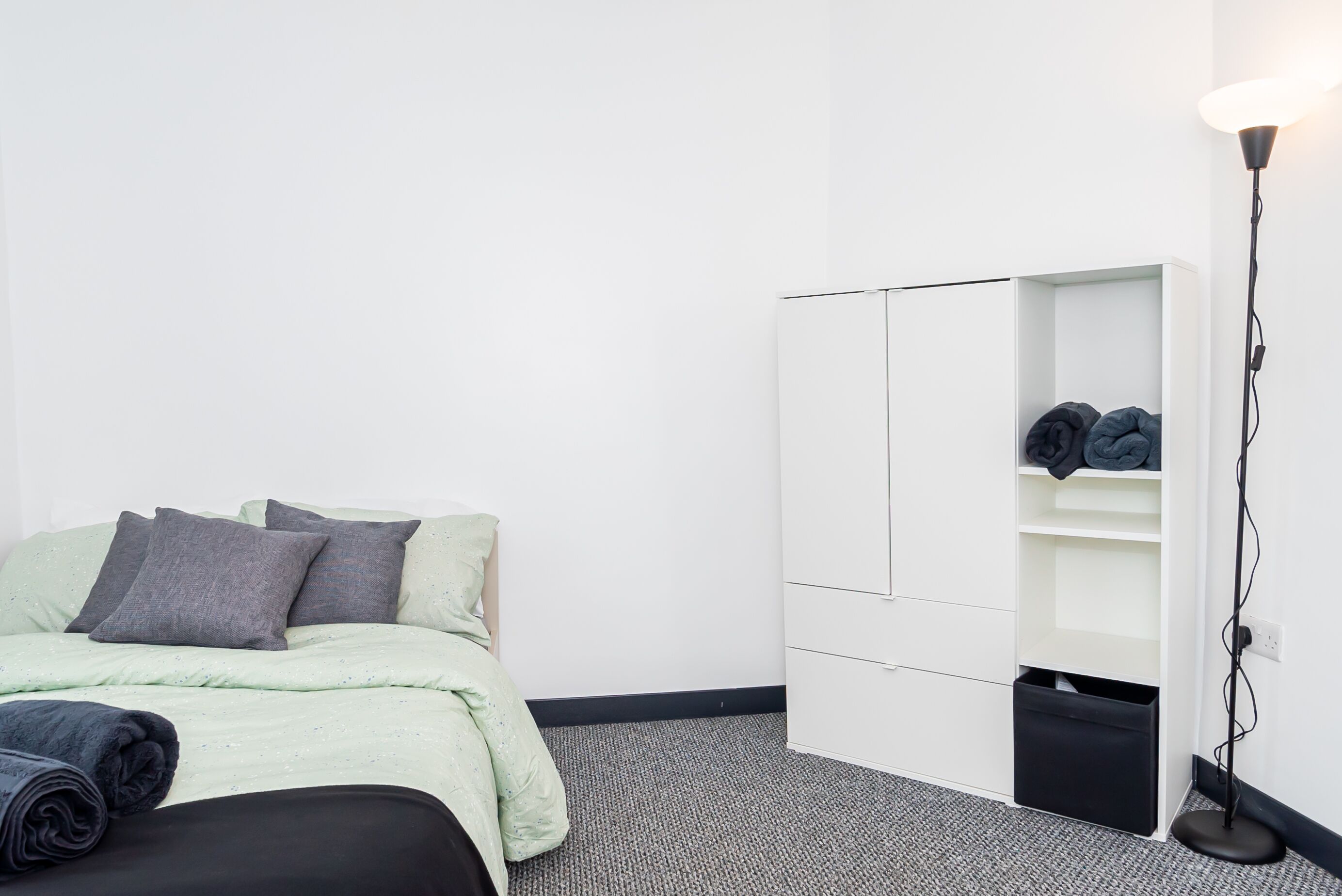 A minimalist bedroom with a bed, a wardrobe, and a floor lamp.