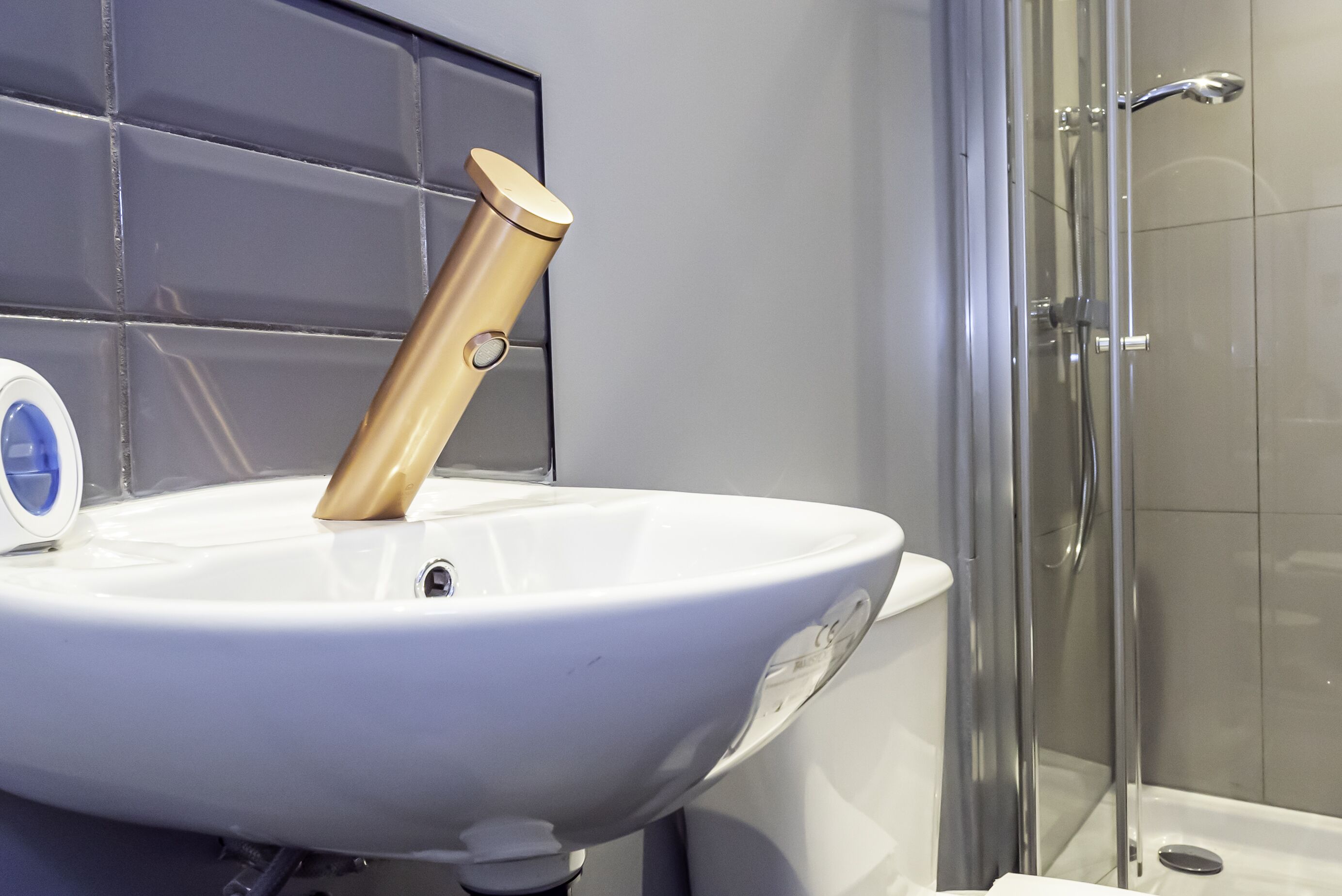 Un baño con lavamanos blanco, grifo dorado y cabina de ducha de vidrio.