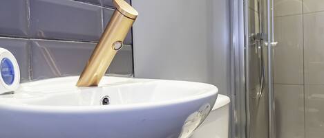 Un baño con lavamanos blanco, grifo dorado y cabina de ducha de vidrio.