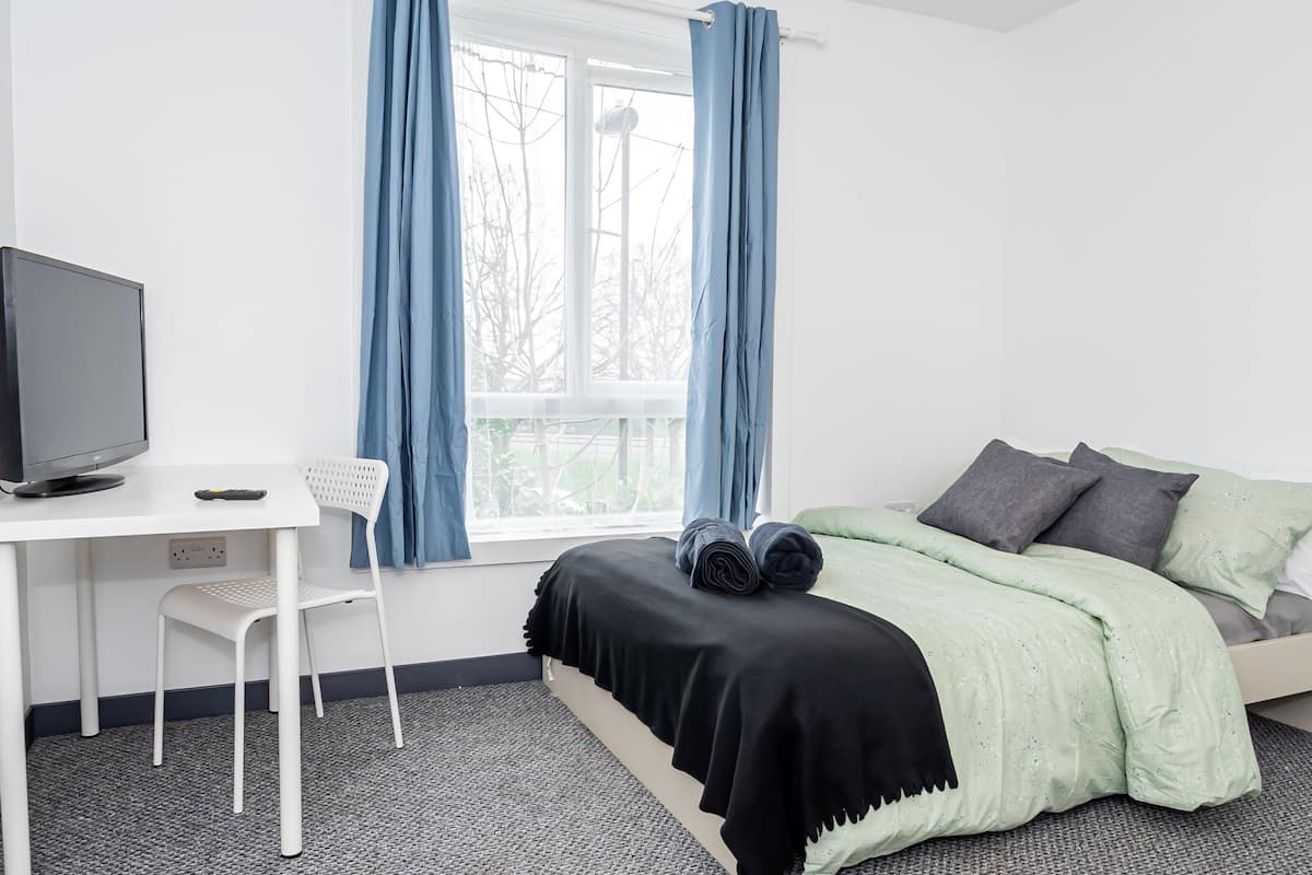 Een slaapkamer met een bed, bureau, stoel en raam met gordijnen.