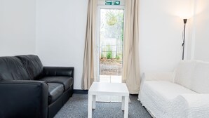 Ein Zimmer mit einer schwarzen Ledersofa, einem weißen Tisch und einem weißen Sofa. Eine Tür mit beigen Vorhängen und ein Ausgangeschild darüber.