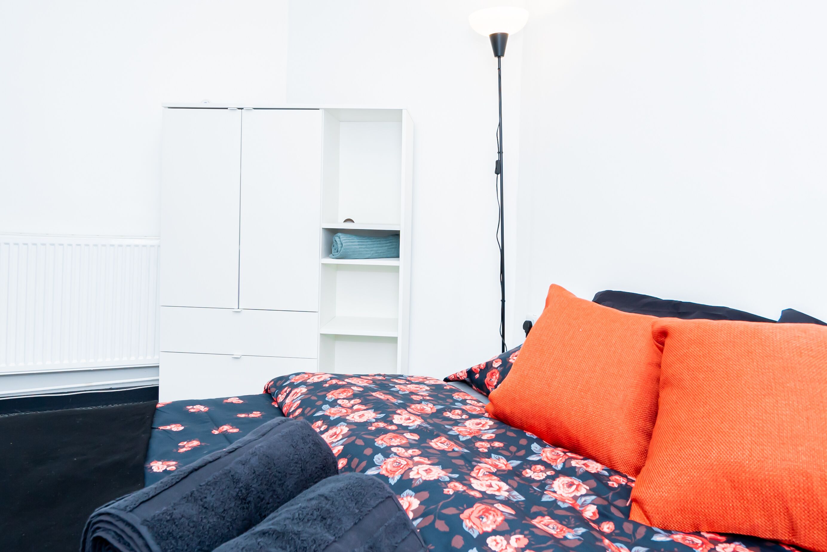 A bedroom with a bed, a wardrobe, and a floor lamp.