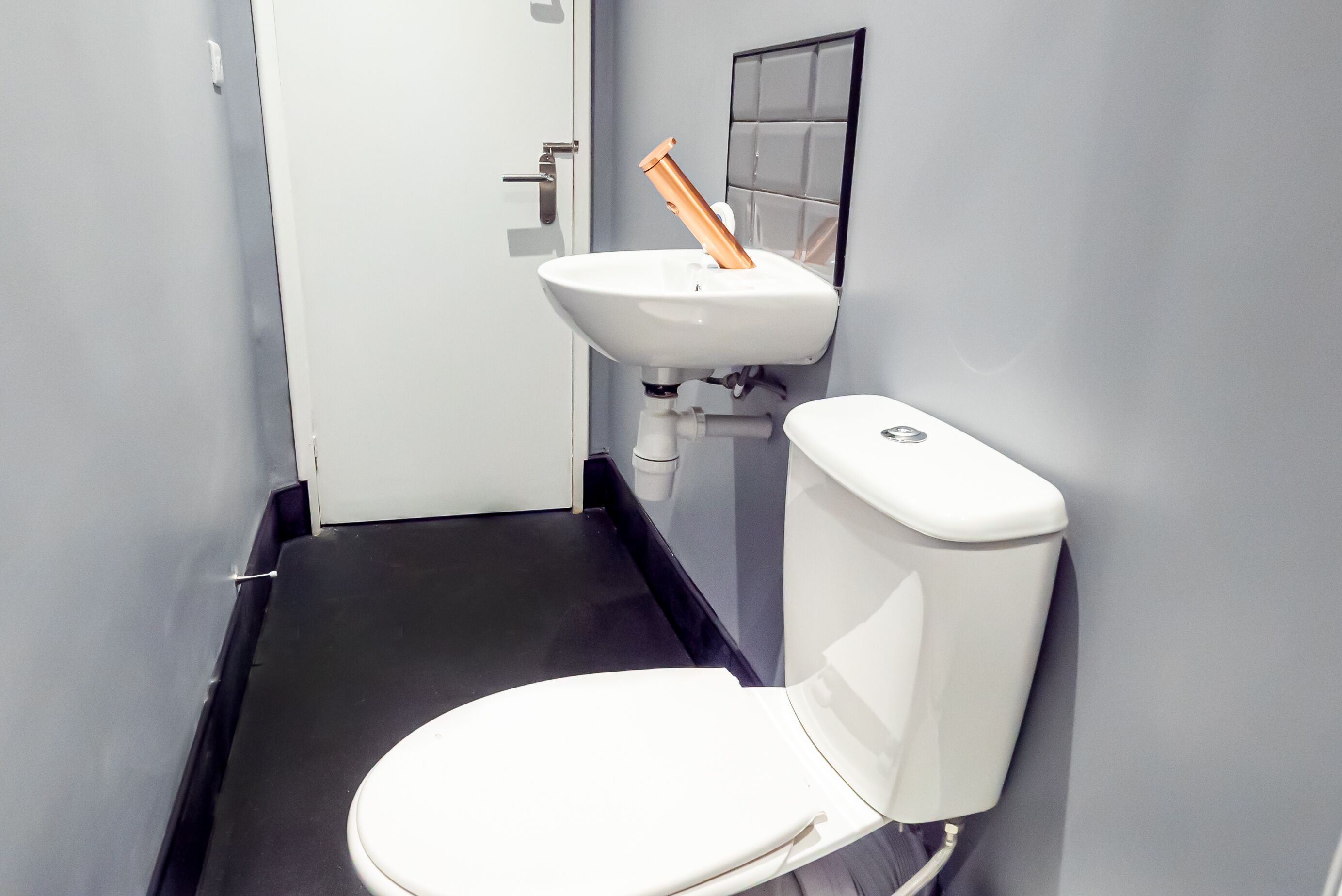Une salle de bain avec des toilettes blanches, un lavabo blanc et un sol noir.