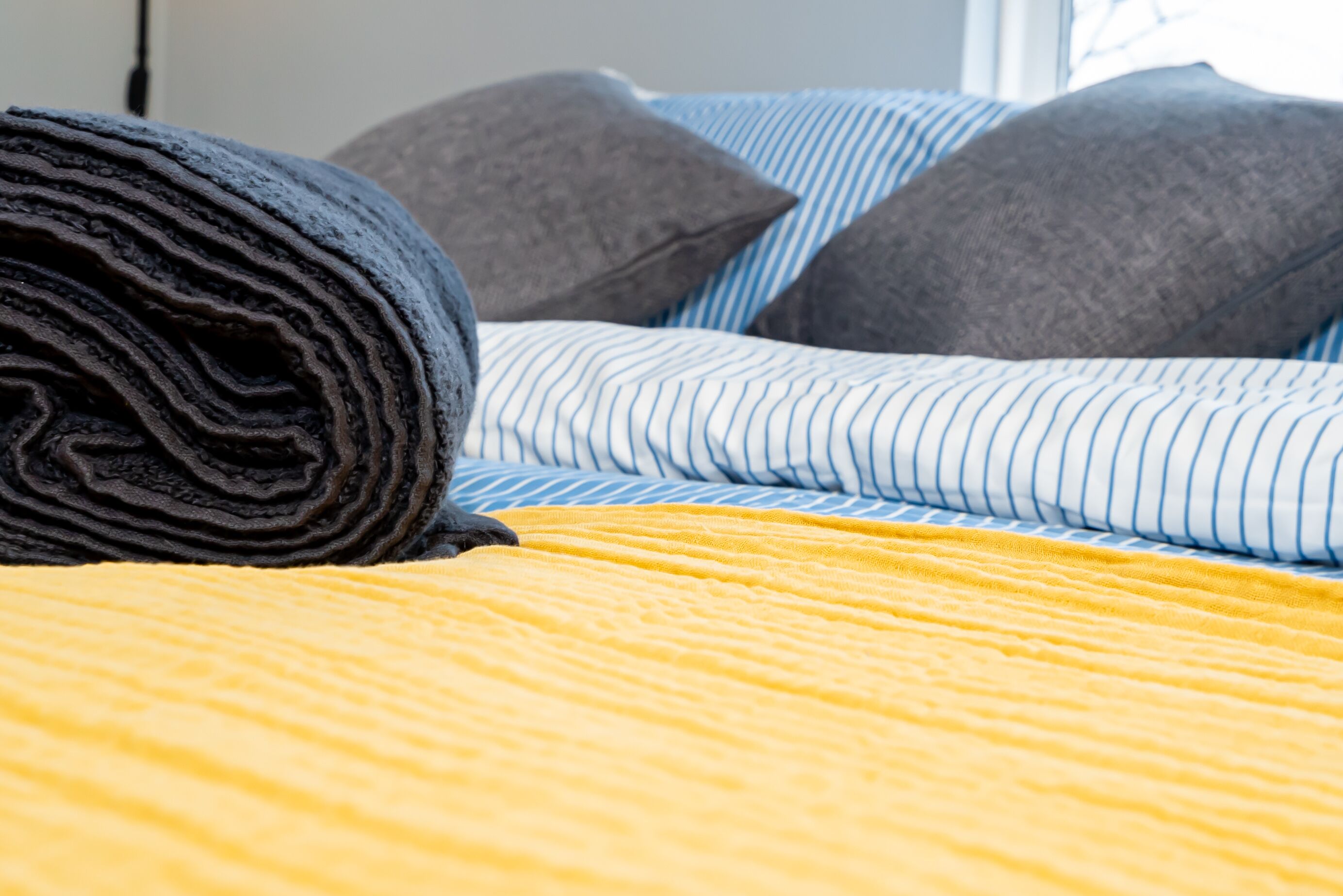 A neatly made bed with striped bedding and rolled-up dark-colored blankets.