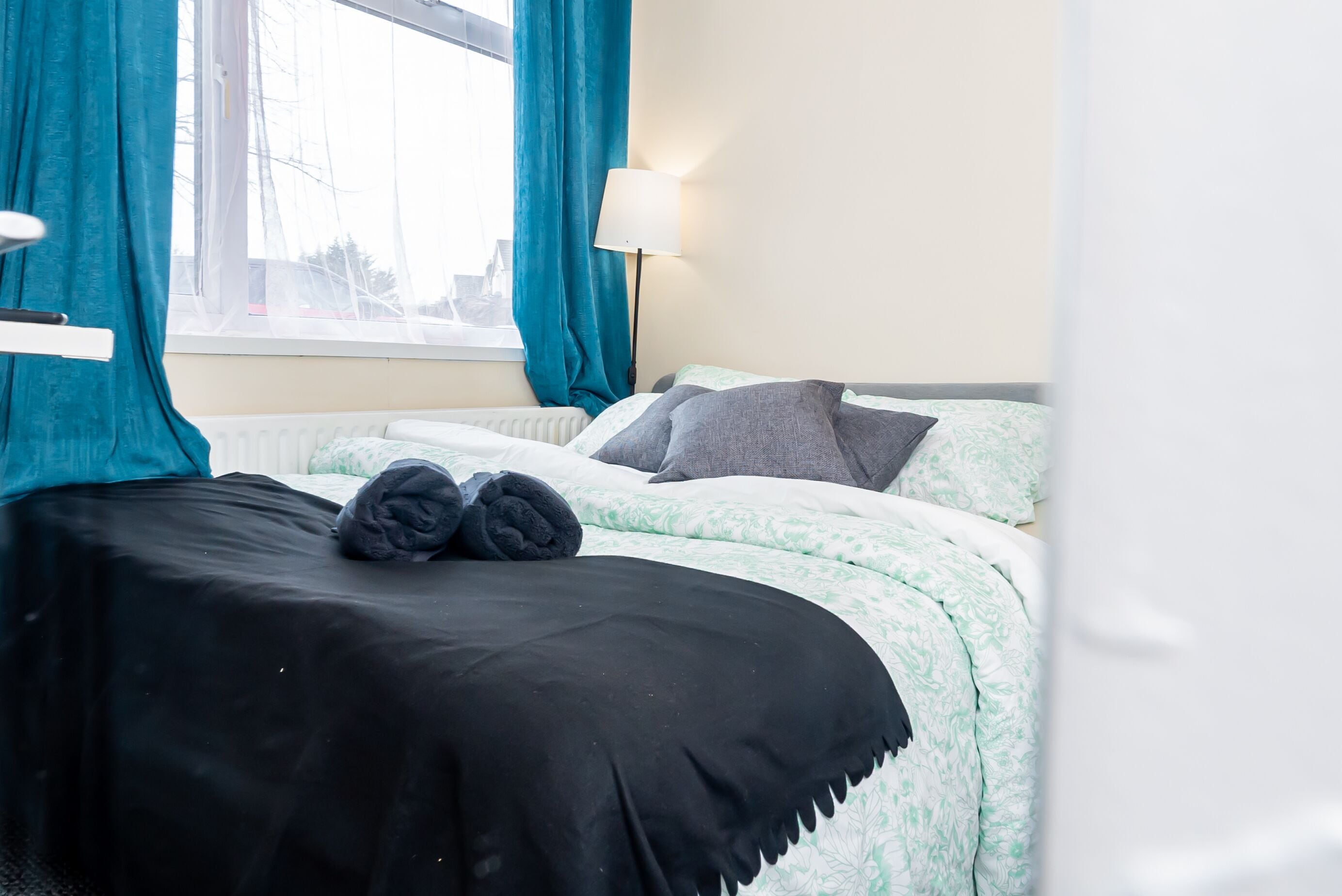 Une chambre d’hôtel avec deux lits, une fenêtre avec des rideaux, une lampe et un radiateur.
