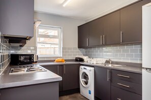 A modern kitchen with grey cabinets, a built-in oven, a microwave, a washing machine, and a window providing natural light. - Shirley House 3 Guest House Self Catering  (Southampton)