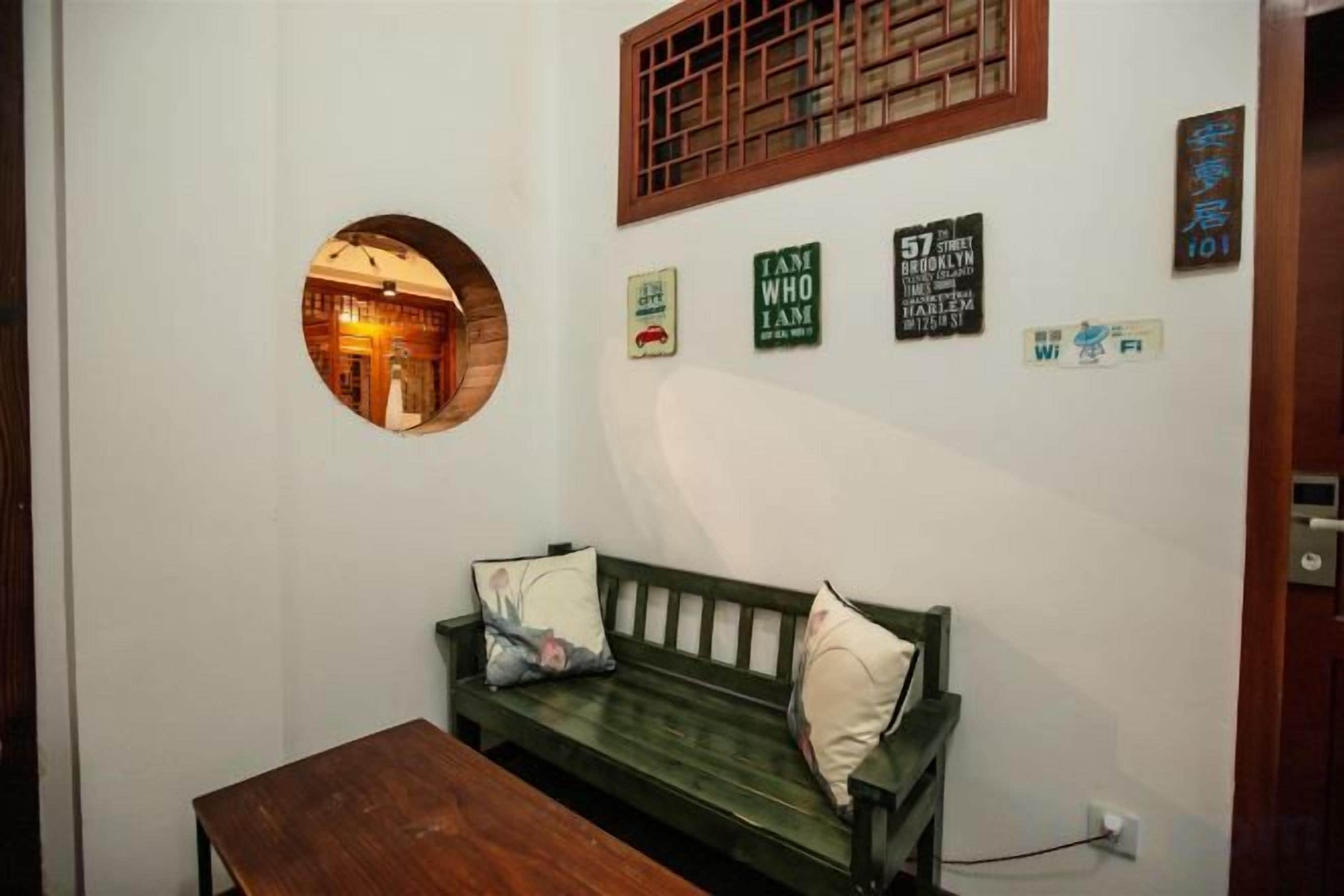Una habitación con un sofá verde, un espejo redondo y una mesa de madera. Se observan decoraciones en la pared y una puerta.
