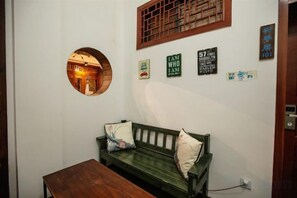 Una habitación con un sofá verde, un espejo redondo y una mesa de madera. Se observan decoraciones en la pared y una puerta.
