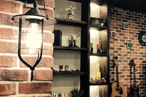 A brick wall with a hanging light fixture, shelves with decorative items, and guitars. - Dream 1988 Hotel (Zhangjiajie)