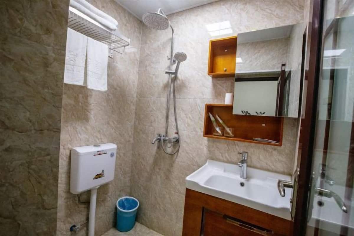 Een badkamer met een marmeren wand, een douche, een wastafel, een spiegel en een handdoekhouder.