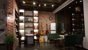 Un salon chaleureux avec un mur en briques, des étagères remplies de divers objets, une guitare et un canapé vert.