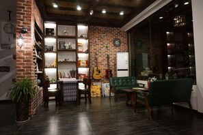 Una sala de estar acogedora con pared de ladrillo, estanterías con diversos objetos, una guitarra y un sofá verde.