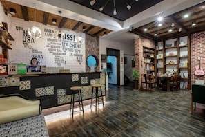 Un espace d’accueil comprenant un comptoir, des tabourets de bar, un mur avec du texte et une bibliothèque en briques.