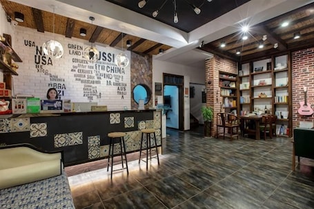 A reception area with a counter, bar stools, a wall with text, and a brick bookshelf.. Dream 1988 Hotel