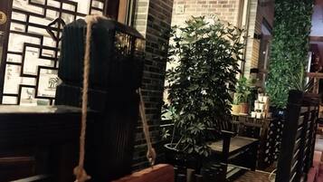 A narrow corridor with a wooden bench, a potted plant, and a brick wall.