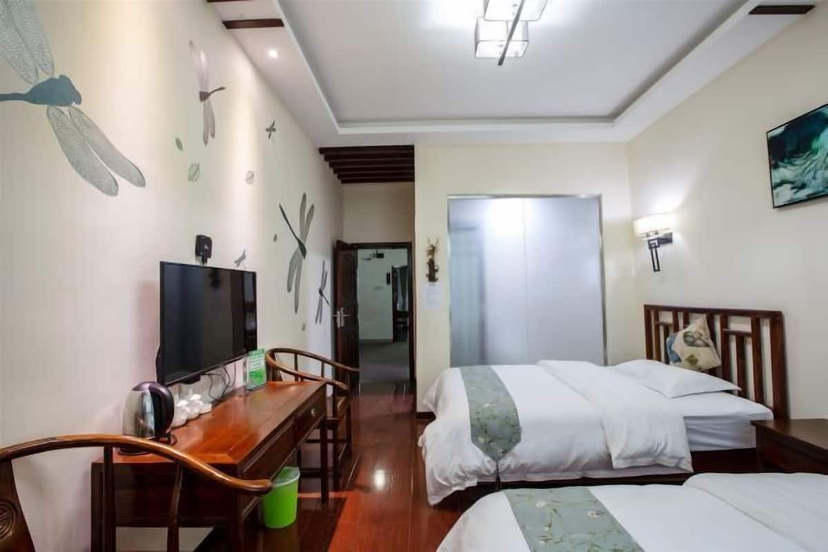 Een hotelkamer met een houten bureau, een flatscreen televisie, twee bedden met witte lakens en een muurschildering van vliegende vogels.