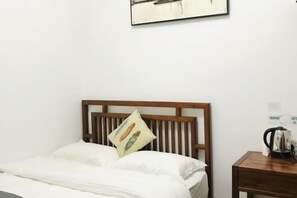 A neatly made bed with a wooden headboard, a pillow with a feather design, and a bedside table with a kettle. - Dream 1988 Hotel (Zhangjiajie)