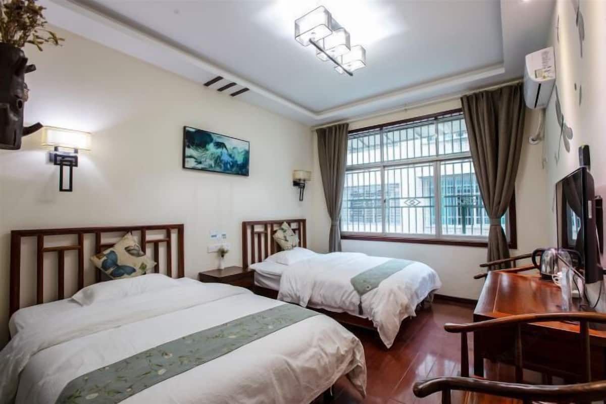 Een hotelkamer met twee bedden, een bureau, een stoel, een televisie, een raam met gordijnen en een schilderij aan de muur.