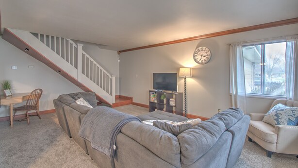 A living room with a staircase, a sofa, a chair, a TV, and a lamp.