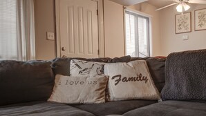 A living room with a dark brown couch, two decorative pillows, a ceiling fan, and a door with a window.