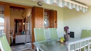 Ein Zimmer mit Glastisch, grünen Stühlen, einer Couch und einem Fenster mit Holzläden.