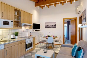 Een moderne keuken met houten kastjes, een magnetron en een eethoek met een tafel en stoelen.