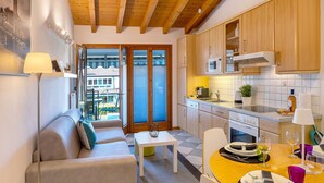 Eine moderne Küche mit Holzausstattung, einem Esstisch mit Stühlen, einer Couch und Blick durch eine Glastür.