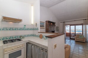 A kitchen with a gas stove, oven, and tiled backsplash. There's a dining area with a sofa and a view of the outside. - Palau Three-Room Apartment with Sea View and Garden "B" (palau)