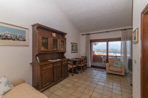 A living room with a wooden cabinet, a dining table, a sofa, and a view through a glass door. - Palau Three-Room Apartment with Sea View and Garden "B" (palau)
