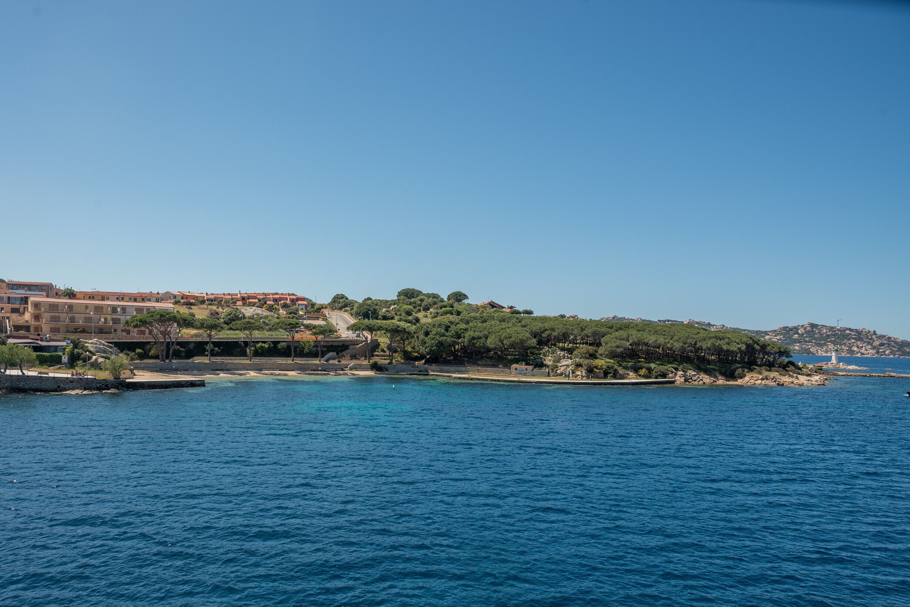 Une ville côtière avec des bâtiments, une mer d’un bleu limpide et un paysage vallonné.