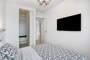 Une chambre à coucher avec un lit, un téléviseur fixé au mur, un dressing et un lustre.