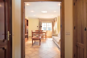An open doorway leading to a living room with a sofa, a dining table with chairs, and a bookshelf.
