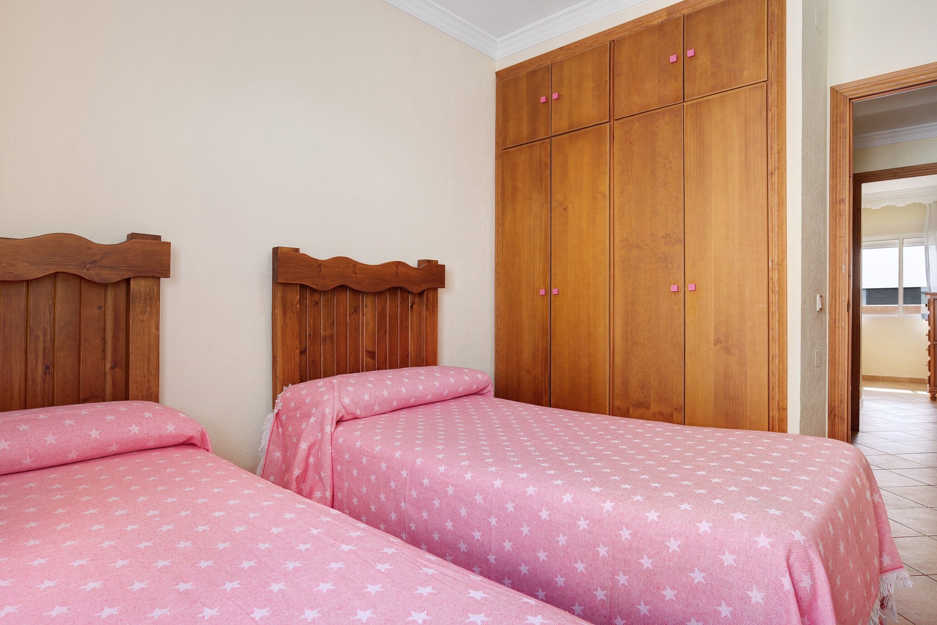 Une chambre avec deux lits, des têtes de lit en bois, une grande armoire et un sol carrelé.