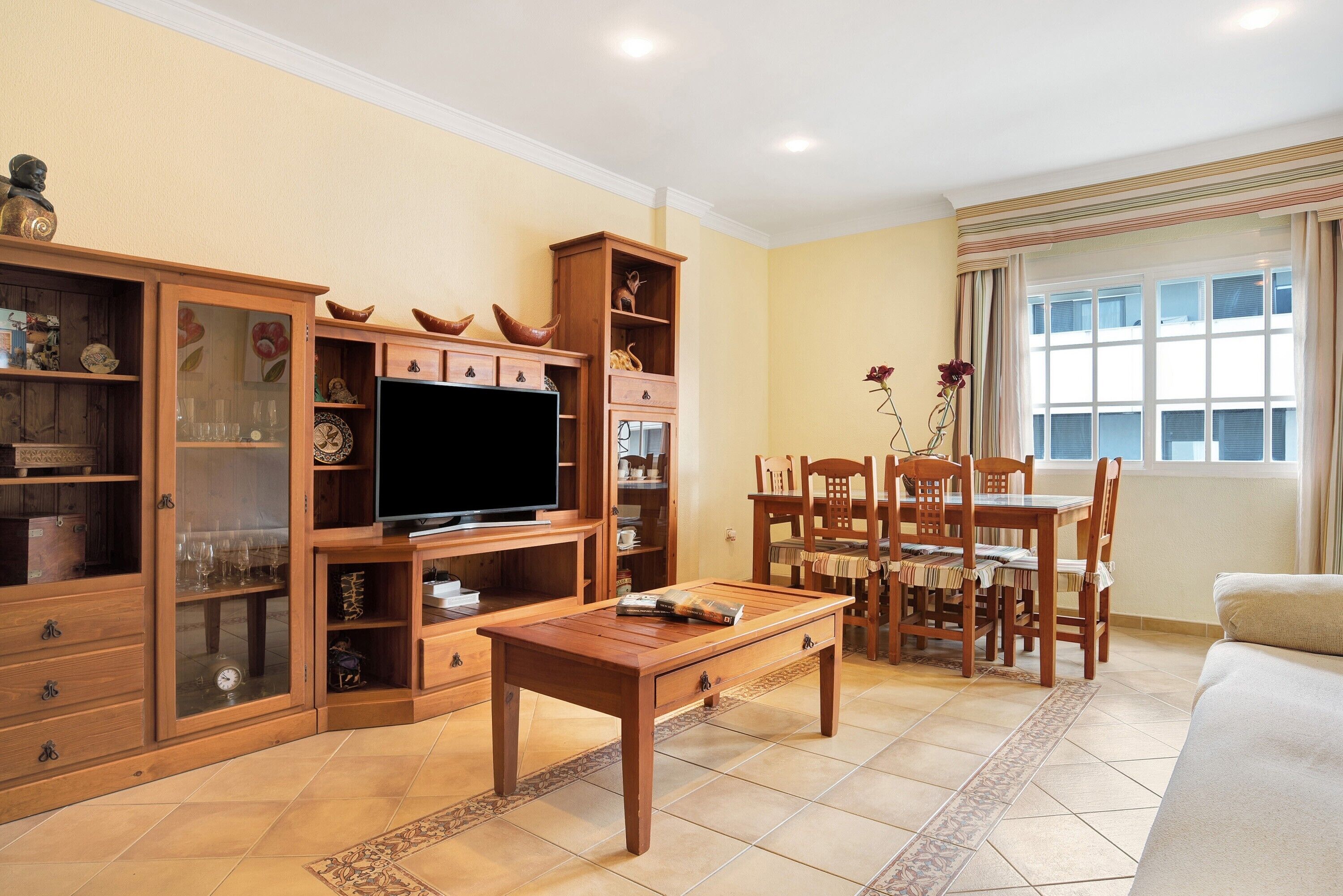 Ein Wohnzimmer mit Fernseher, Holzmöbeln, einem Esstisch mit Stühlen und einem Sofa.