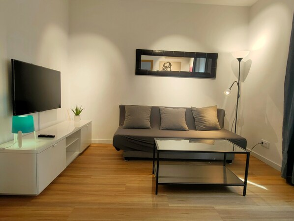 A modern living room with a flat-screen TV, a sofa, a coffee table, and a floor lamp.