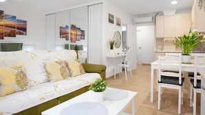 A modern living room with a sofa, a dining table, and chairs. There is a small table with a plant and a mirror on the wall. - Studio Apartment "Loft Centro Historico Barbate" close to the Sea with Wi-Fi (Barbate)