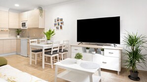 A modern living room with a flat-screen TV, dining table, chairs, and a potted plant. - Studio Apartment "Loft Centro Historico Barbate" close to the Sea with Wi-Fi (Barbate)