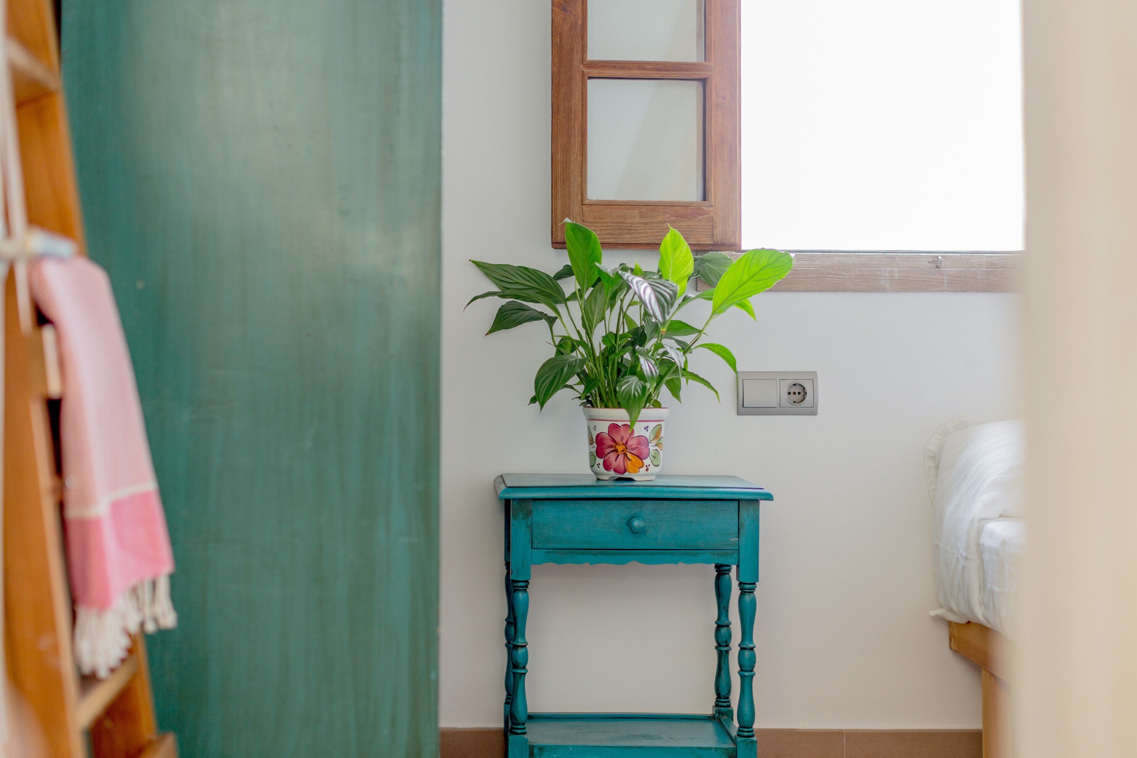 Un bagno con un mobile lavabo color petrolio, una pianta in vaso, una finestra e un portasciugamani.