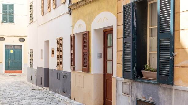 Una estrecha calle adoquinada con edificios que tienen puertas arqueadas y contraventanas.