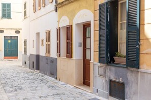 Eine enge Kopfsteinpflasterstraße mit Gebäuden, die Rundbogenportale und Fensterläden aufweisen.