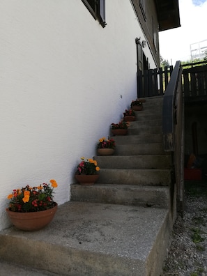 Une série de marches en béton menant à un bâtiment blanc, agrémenté de rampes noires et de plantes en pot sur chaque marche.