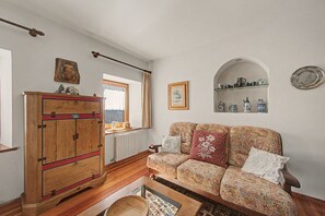 A room with a wooden wardrobe, a patterned sofa, a radiator, and a window with curtains.