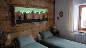Ein Schlafzimmer mit einem hölzernen Kopfteil, einem Bett mit zwei Kissen, einem Nachttisch mit einer Lampe und einem Wandbild mit einer Waldszene.