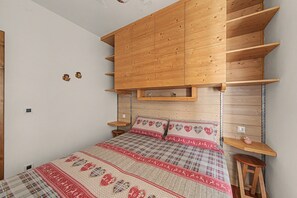 Una camera da letto con una testiera in legno, un letto con copriletto fantasia, un comodino in legno e uno scaffale fissato al muro.