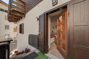 Eine Holztür mit dekorativer Glasscheibe, eine kleine Veranda mit einer Bank und einer an der Wand befestigten Leuchte.
