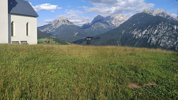 Eine Kirche mit einem Glockenturm, umgeben von einer Wiese und Bergen.