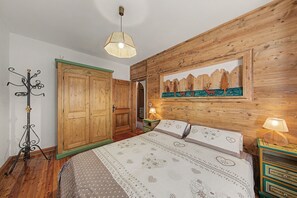 Un dormitorio con cabecera de madera, cama con ropa de cama estampada, mesita de noche con lámpara y un cuadro colgado en la pared.
