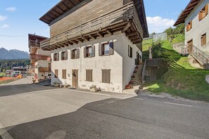 Un edificio tradizionale con tetto spiovente, diverse finestre con persiane e una scala che conduce a un piano superiore.