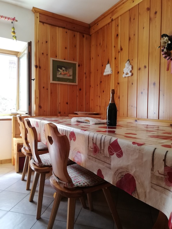 Une pièce aux murs lambrés, avec une table  à manger, des chaises, une bouteille et un tableau encadré accroché au mur.